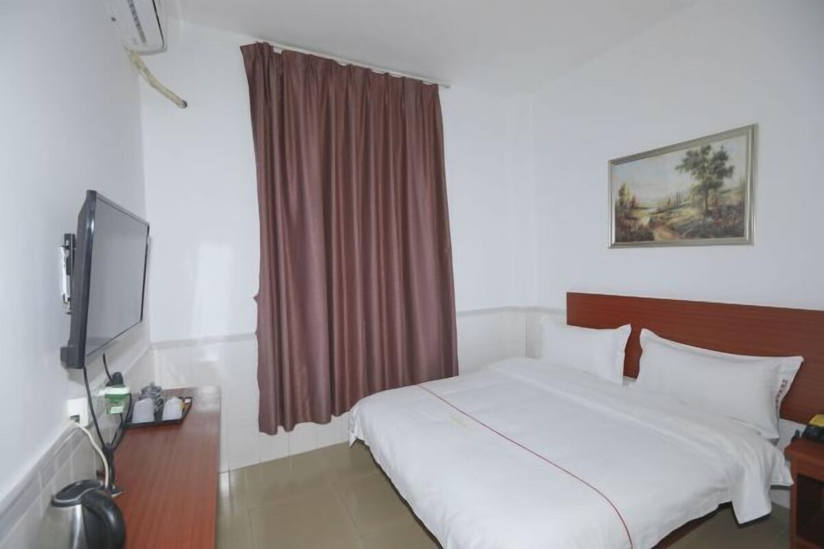 Una habitación de hotel con cama, televisión, un cuadro en la pared y una ventana con cortinas.