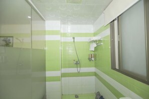 Un baño con azulejos verde y blanco a rayas, mampara de vidrio y ventana.