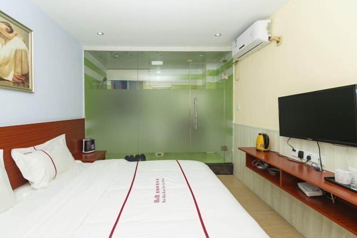 Habitación de hotel con cama, televisión, espejo y zona de ducha.