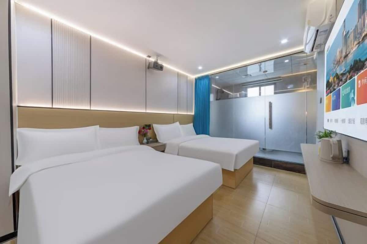 A hotel room with two beds, a desk, a mirror, and a shower area.