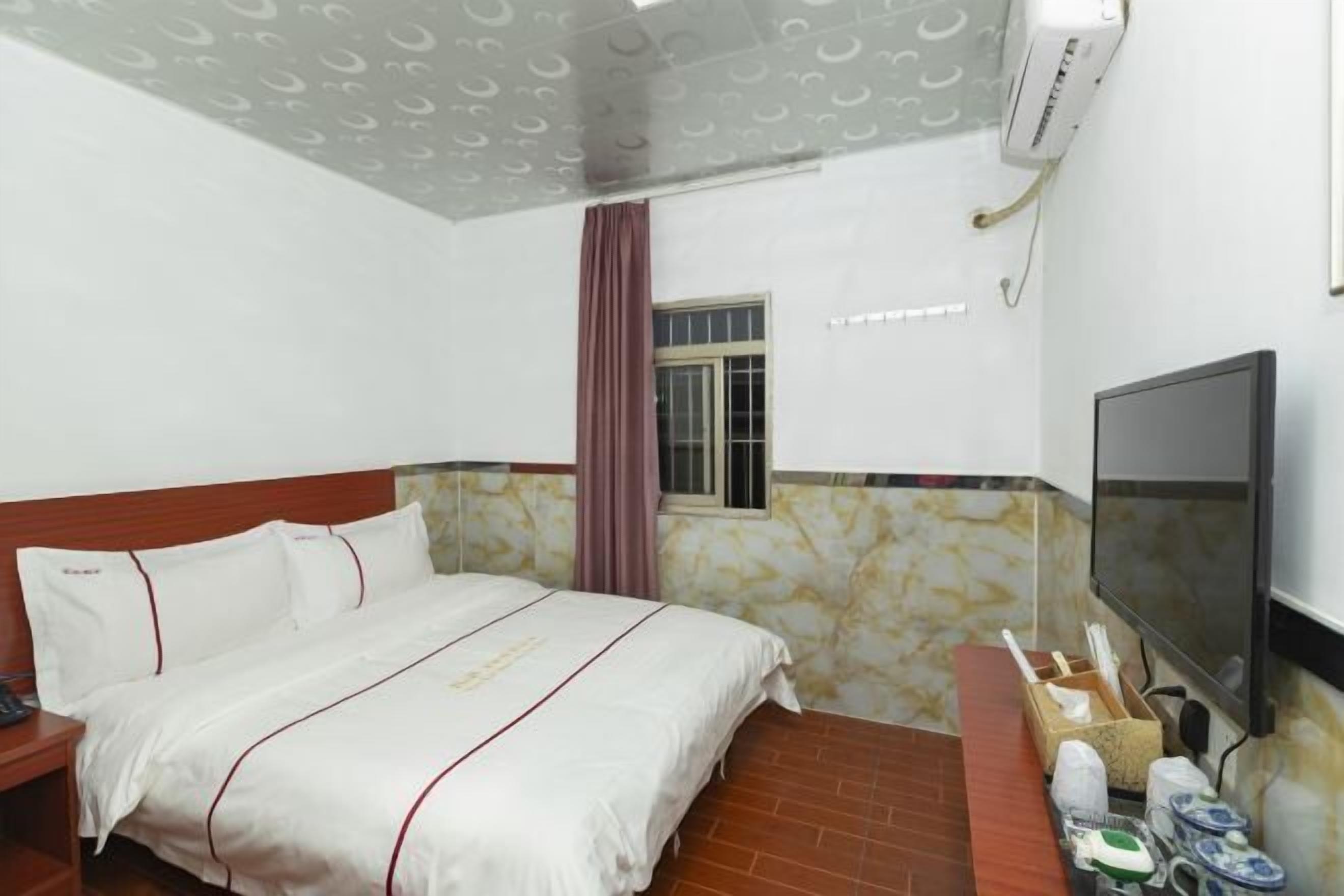 A hotel room with a bed, a TV, a window with curtains, and a bathroom area with toiletries.