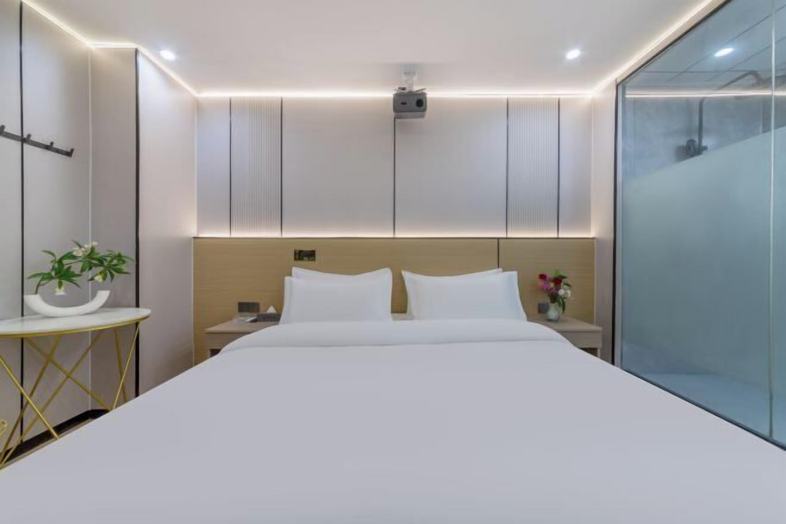 A modern hotel room with a large bed, bedside tables, a wall-mounted TV, and a glass shower enclosure.