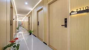 Un corridoio d'hotel con porte in legno, una targa con il numero 8310 e piante in vaso lungo il pavimento.