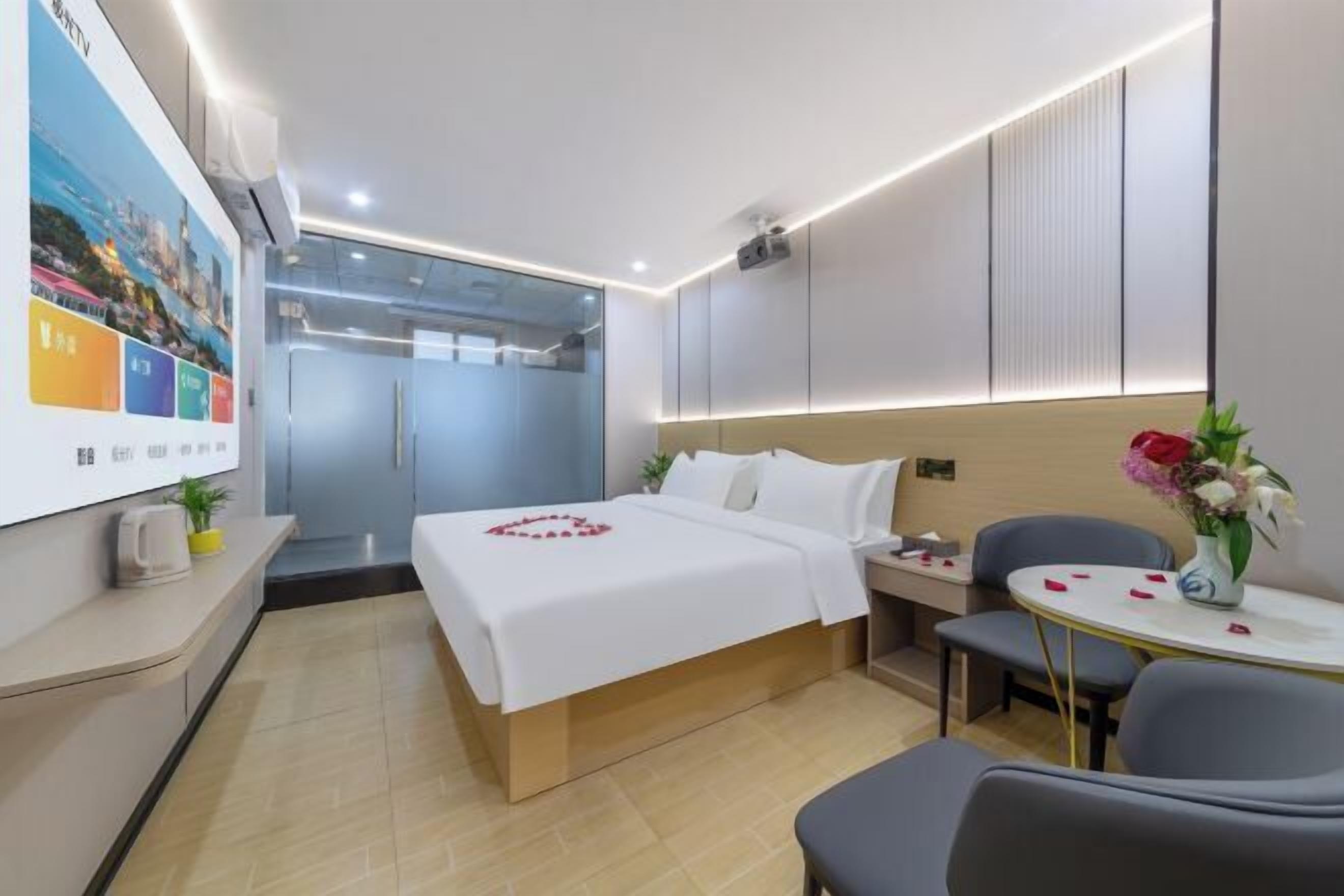 A hotel room with a bed, bedside table, chair, and a small table with flowers.