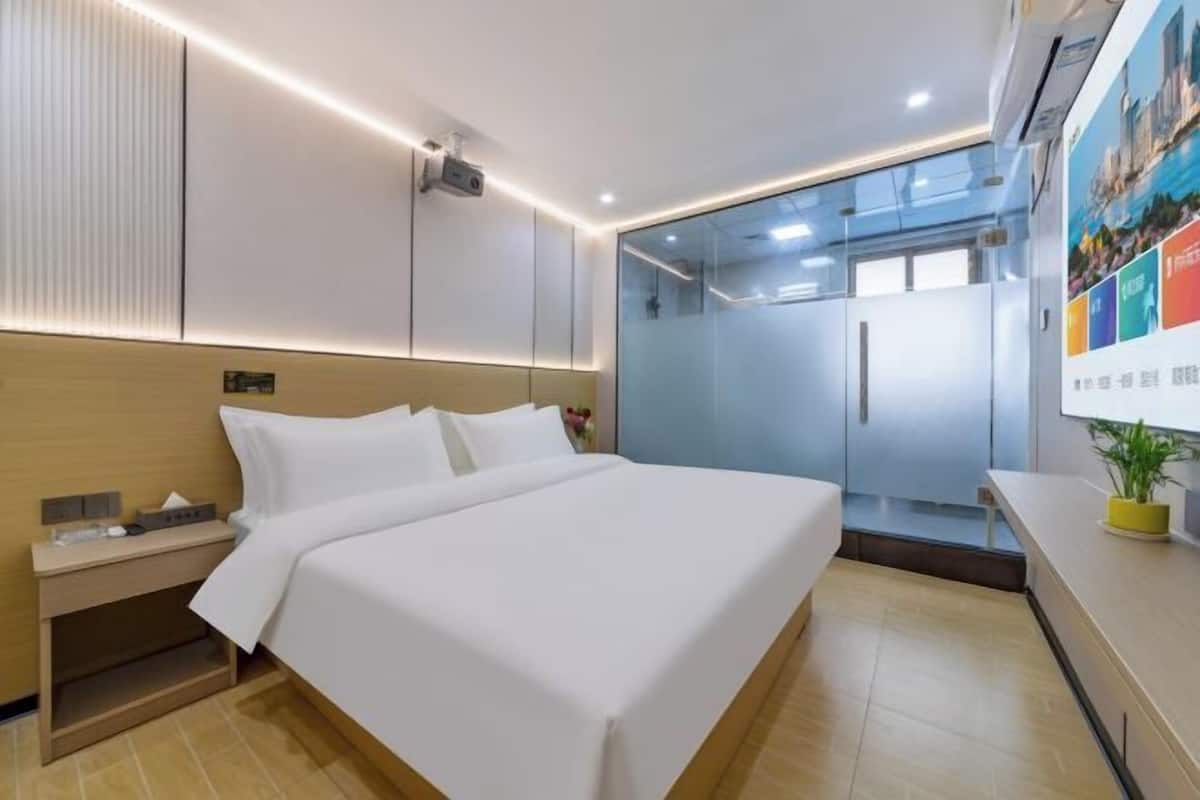 A modern hotel room with a bed, bedside table, and a glass partition wall.