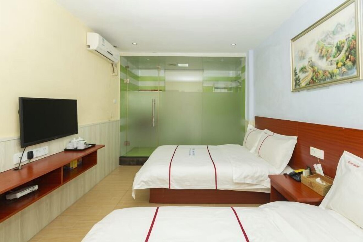 Habitación de hotel con dos camas, televisión, un cuadro y zona de ducha.