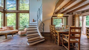 Ein Holzinterieur mit einer Wendeltreppe, einem Essbereich und großen Fenstern mit Blick ins Freie.