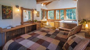 Ein gemütliches Schlafzimmer mit einem großen Bett, einem Holzkopfende, einem Fenster mit Blick auf Bäume und einem kleinen Badezimmer mit einer Badewanne.