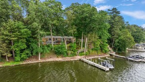 A lakeside property with a dock, surrounded by dense trees and a two-story building with a balcony.