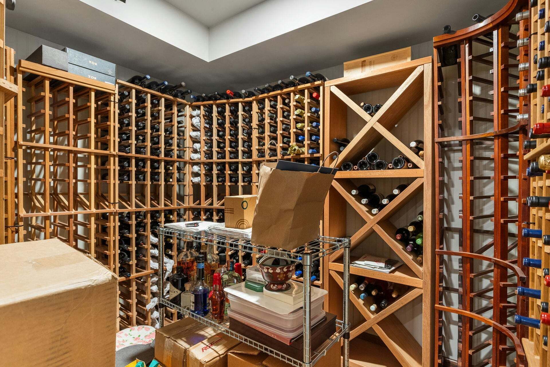 Una cantina vinicola con numerose scaffalature in legno piene di bottiglie di vino, uno scaffale metallico con diversi oggetti e scatole di cartone.