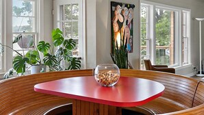 A dining area with a round wooden table and chairs, a ceiling fan, and large windows.