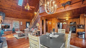 A spacious wooden cabin with a dining area, kitchen, and a staircase leading to upper levels.
