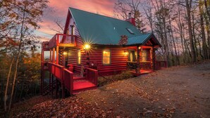 A log cabin with a red exterior, a porch, and a chimney.