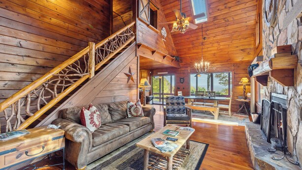 A log cabin interior with a wooden staircase, leather sofa, dining table, and fireplace.
