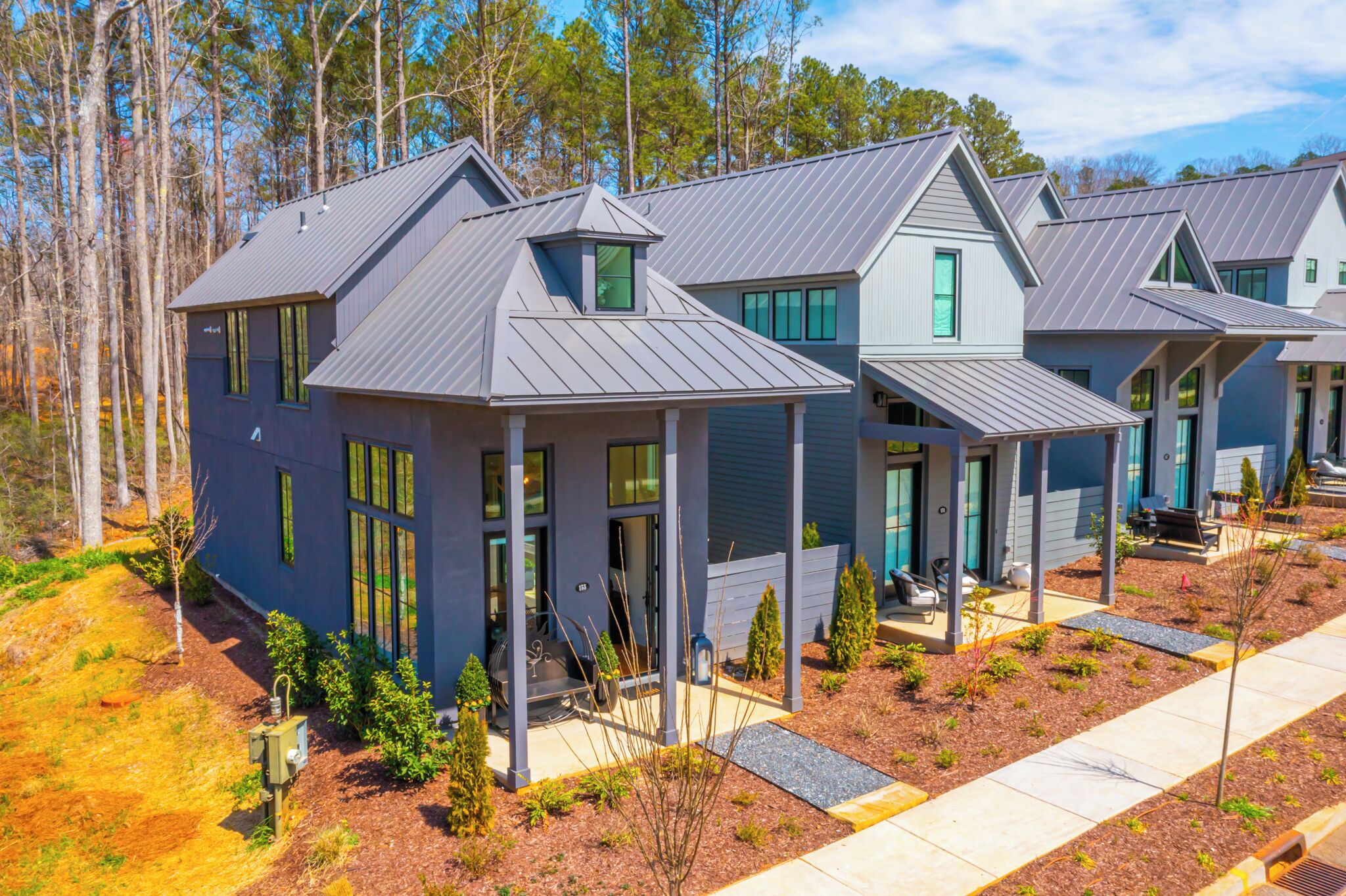 A modern residential building with a metal roof, large windows, and a well-maintained lawn.