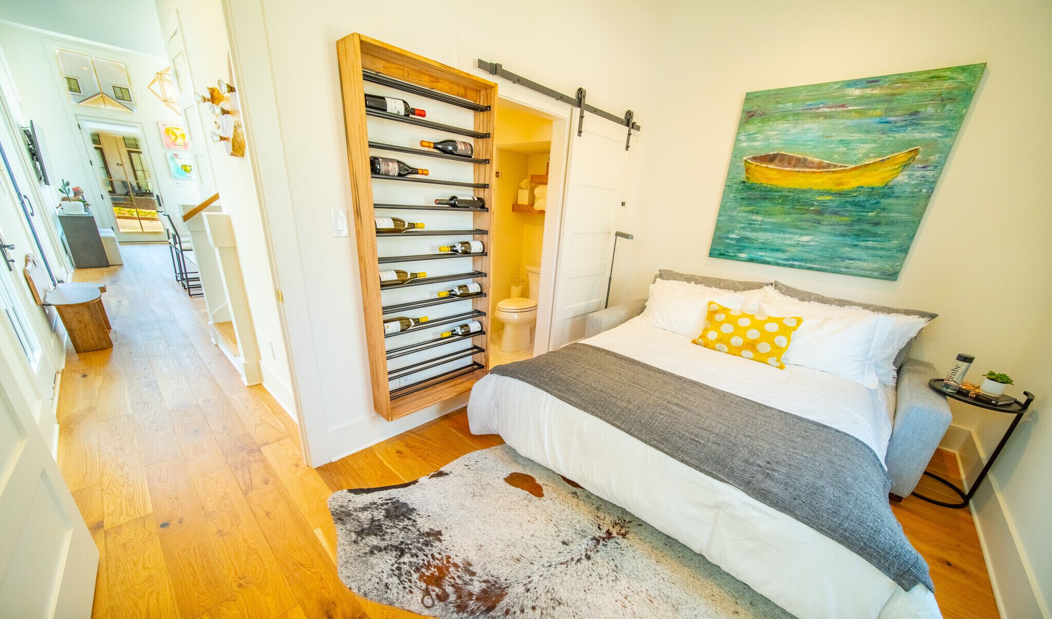 A bedroom with a bed, a wooden wine rack, a painting of a boat, and a view of a balcony.