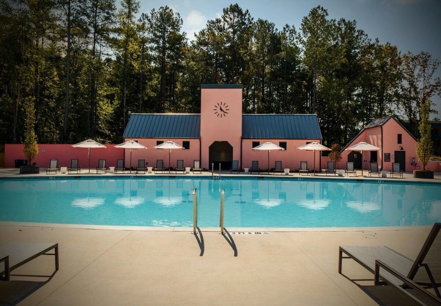 A swimming pool with lounge chairs and umbrellas, surrounded by a building with a clock tower.