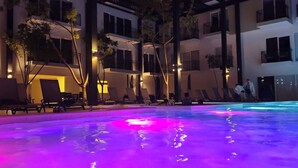 A swimming pool with colorful lighting, surrounded by lounge chairs and trees, with a building in the background. - Casa de Elena – Tranquility, Peace & Relaxation (Bucerias)