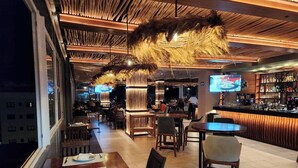 A restaurant with wooden tables and chairs, a bar area, and a TV screen displaying a program. - Casa de Elena – Tranquility, Peace & Relaxation (Bucerias)