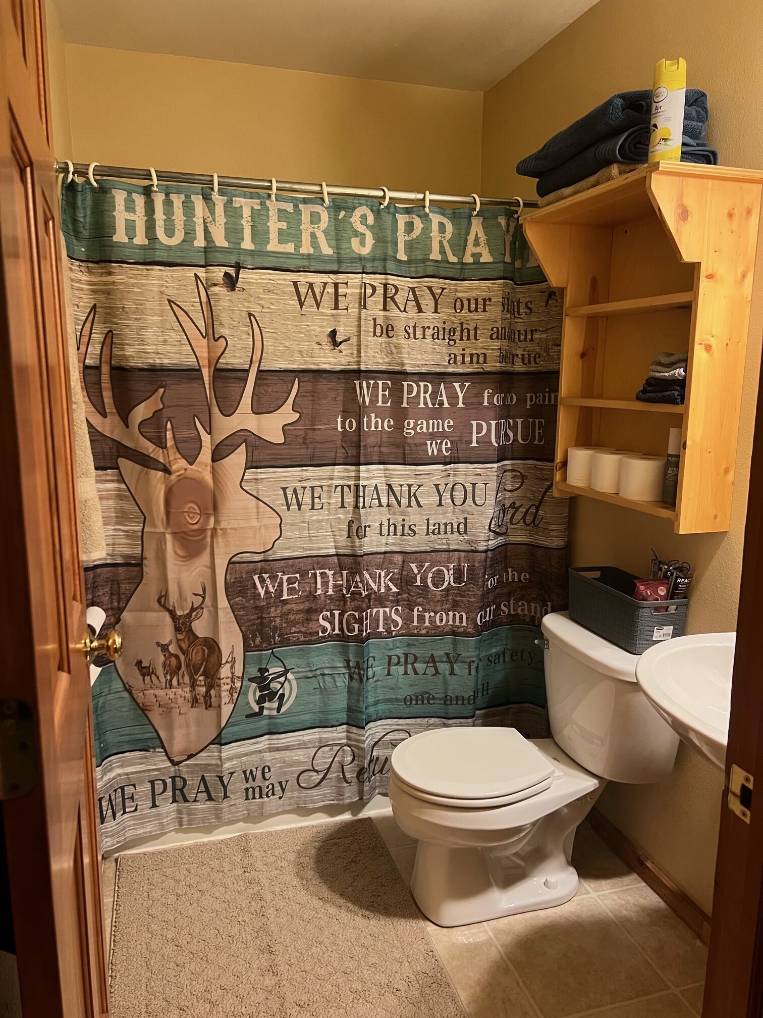 Un baño con cortina de ducha alusiva a la caza, un inodoro y un estante de madera con artículos de aseo.