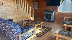 A wooden cabin interior with a staircase, a fireplace, a television, and patterned furniture. - Cozy 3 Bed 2 Bath Cabin located next to Three Bears Resort in Warrens Wisconsin  (Warrens)