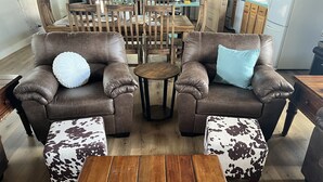 A living room with two brown leather sofas, a wooden coffee table, and cowhide-patterned ottomans. - Hill Country Lodge * Great for Groups & Multi Family Gatherings (Doss)