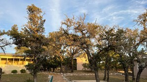 A courtyard with a hammock, trees, and a building with a star emblem. - Hill Country Lodge * Great for Groups & Multi Family Gatherings (Doss)