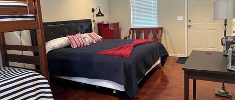 Un dormitorio con una cama litera, una cama individual, un escritorio, una silla, una lámpara y una ventana con persianas.