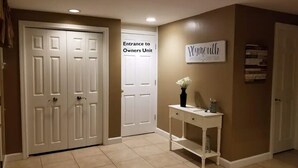 Un couloir avec une porte blanche portant l’inscription « Entrée de l’unité réservée aux propriétaires », une console blanche sur laquelle est posé un vase, et une pancarte indiquant « Plymouth ».