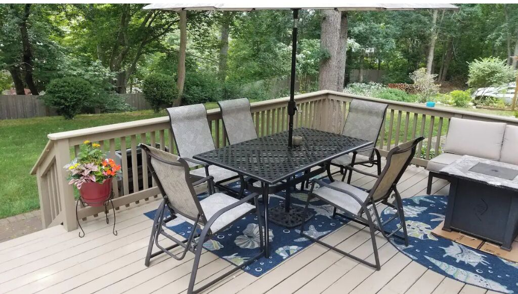 Een terras met een metalen tafel en stoelen, een bloempot en een barbecue.