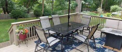 Een terras met een metalen tafel en stoelen, een bloempot en een barbecue.