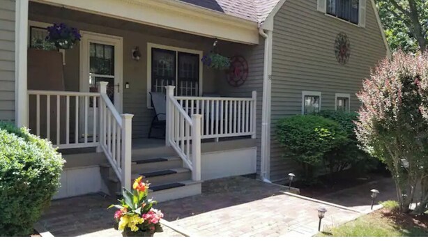 Une maison à deux étages avec un porche à l’avant, un escalier et un petit jardin.