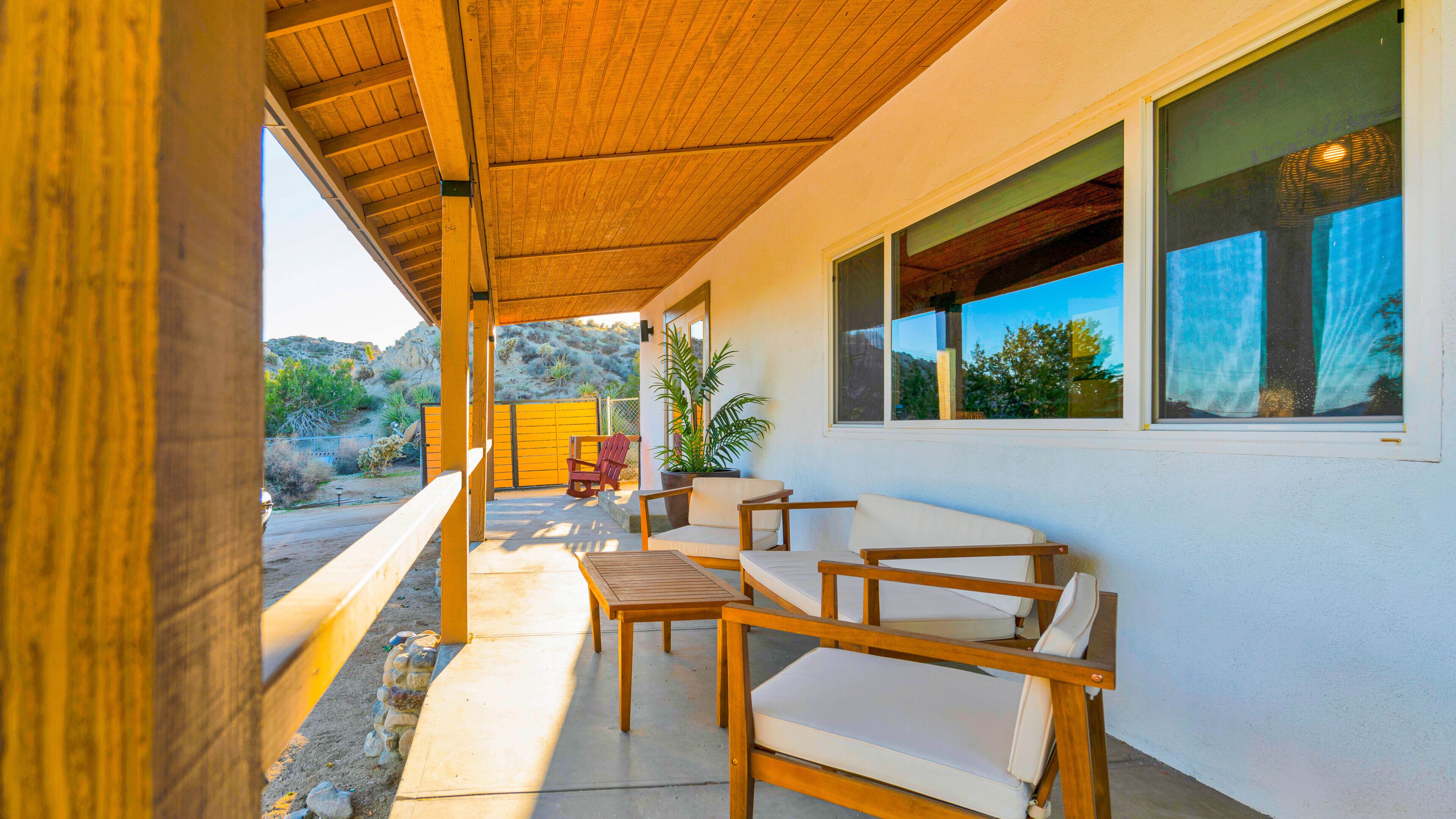 Un patio cubierto con muebles de madera, una planta en maceta y vistas del paisaje circundante.