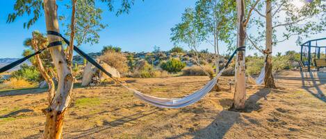 A hammock between trees in a dry, rocky landscape with a clear sky.