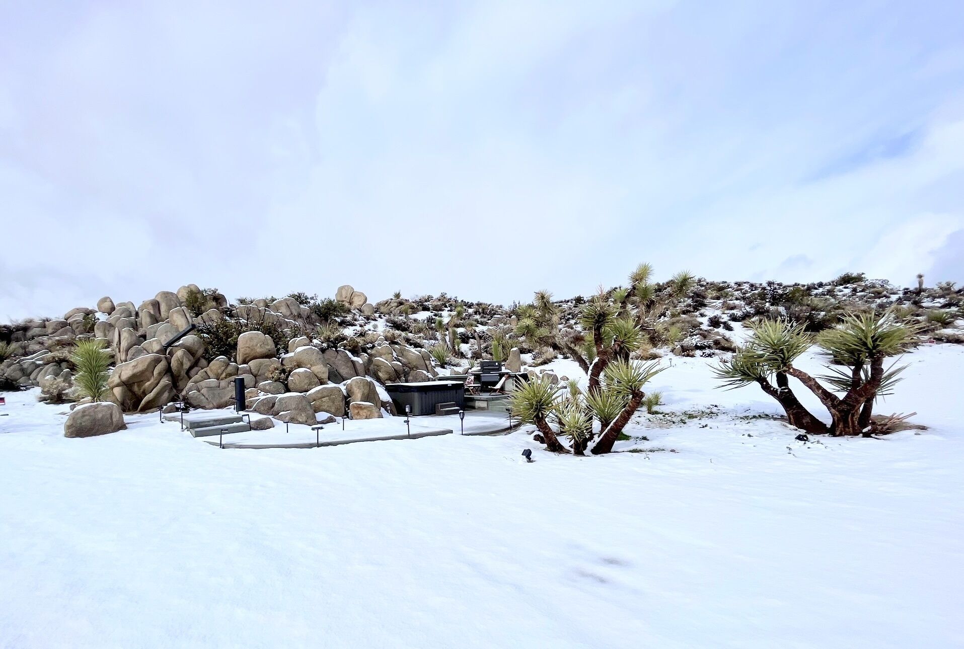 A desert landscape with large rocks, sparse vegetation, and a clear sky.
