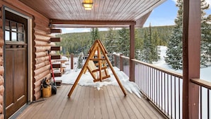 A wooden deck with a wooden swing set, a metal railing, and a view of a snowy forest. - Amazing Secluded Cabin On 10 Acres, Close To Breck (Fairplay)