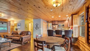 A cozy log cabin interior with a wooden dining table, chairs, a leather sofa, and a kitchen area with modern appliances. - Amazing Secluded Cabin On 10 Acres, Close To Breck (Fairplay)