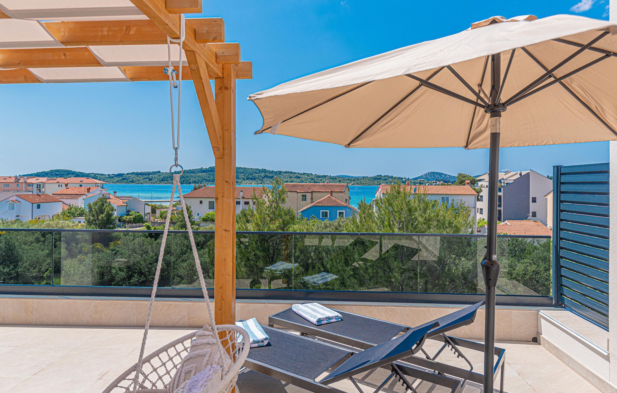 A balcony with a swing chair, two lounge chairs, and a large umbrella.