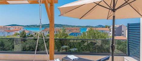 Ein Balkon mit einer Schaukel, zwei Liegestühlen und einem großen Sonnenschirm.