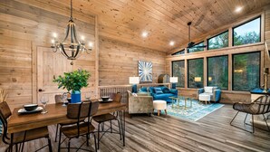 A wooden interior with a dining area, sofas, and large windows. - Perfect Modern Cabin for Couples Hot Tub Indoor Fireplace Pet friendly (Sevierville)