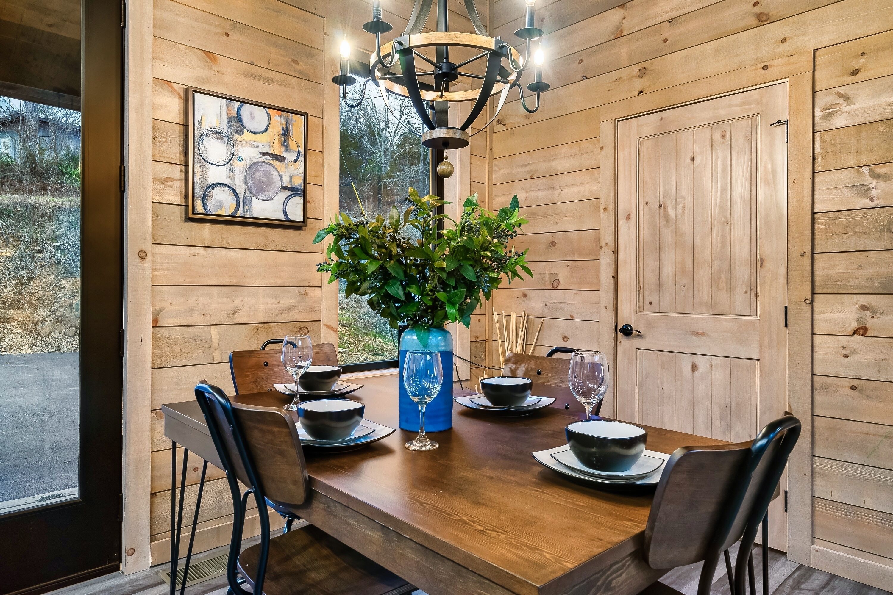 Ein Esszimmer mit Holzwänden, gedecktem Tisch für vier Personen, einer blauen Vase mit Grünpflanzen und einer Kristallleuchter.
