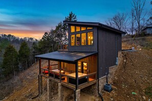 A modern two-story cabin with a balcony, large windows, and a hot tub.