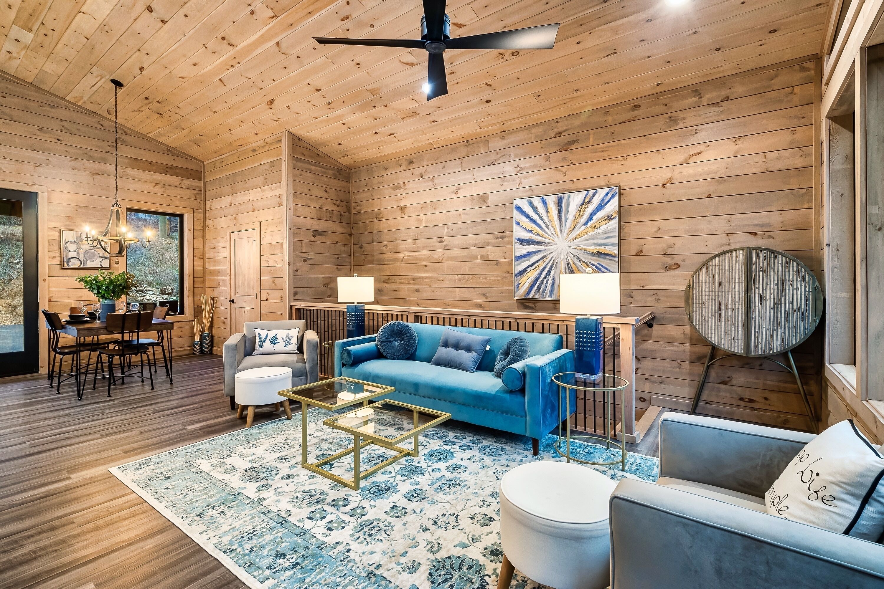 A cozy wooden interior with a blue sofa, a dining area, and a ceiling fan.