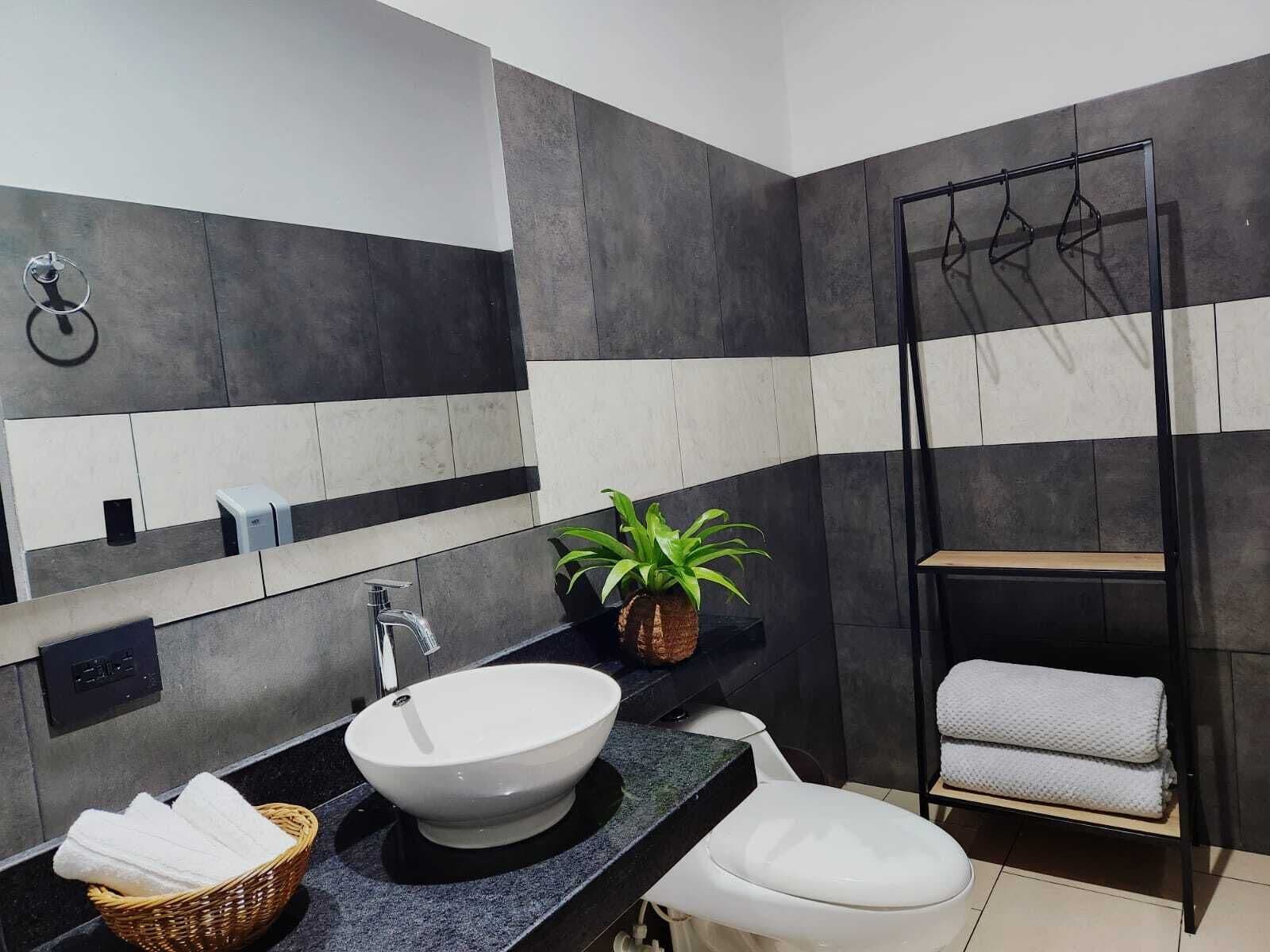 A modern bathroom with a large mirror, a white sink, a toilet, and a towel rack.