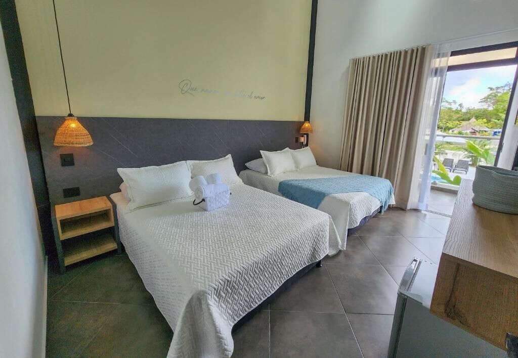 Een hotelkamer met twee bedden, een kleine tafel, een nachtkastje en uitzicht op de omgeving.