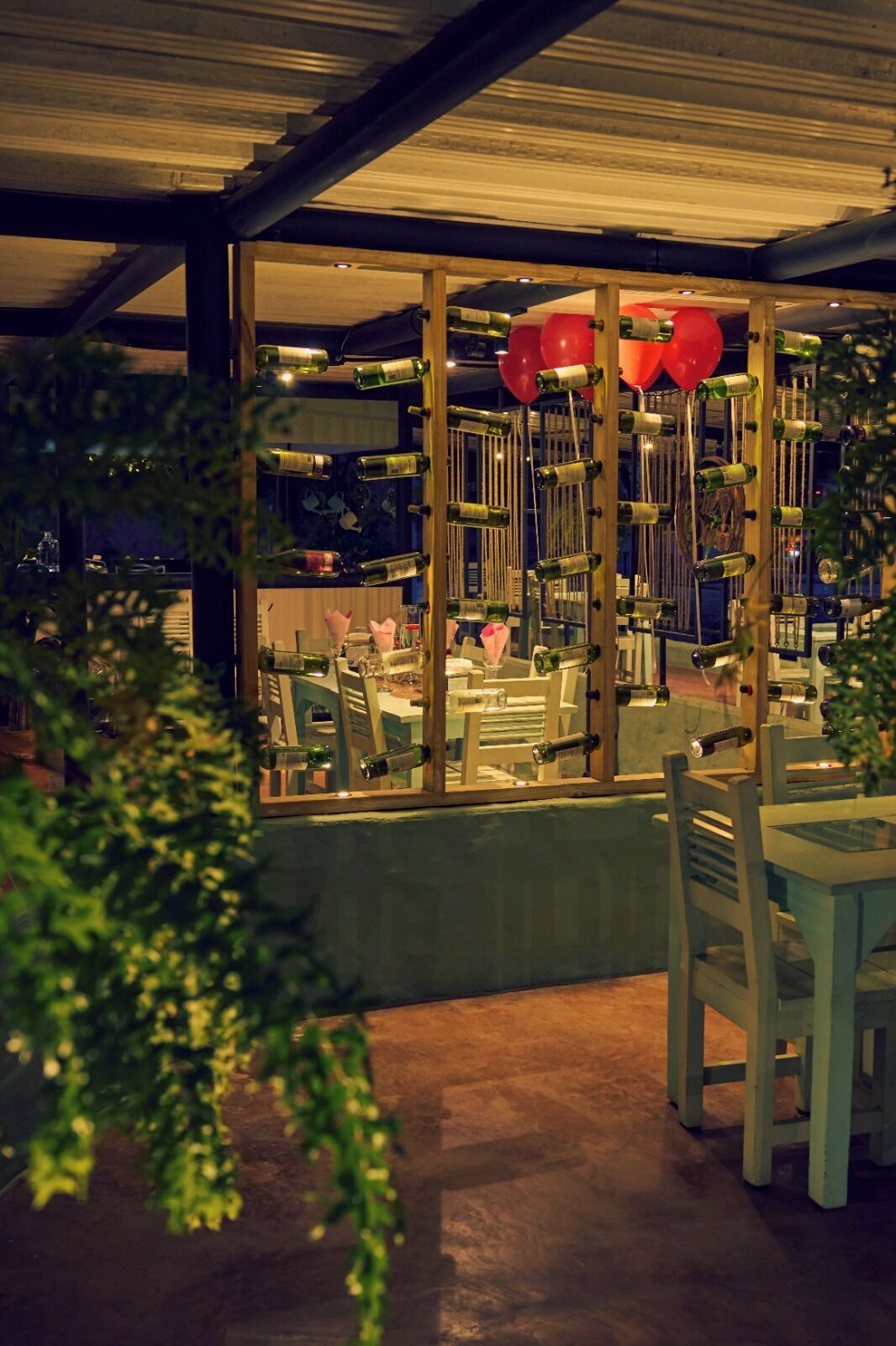 Un restaurante con cerramiento de vidrio, mesas, sillas y globos rojos.