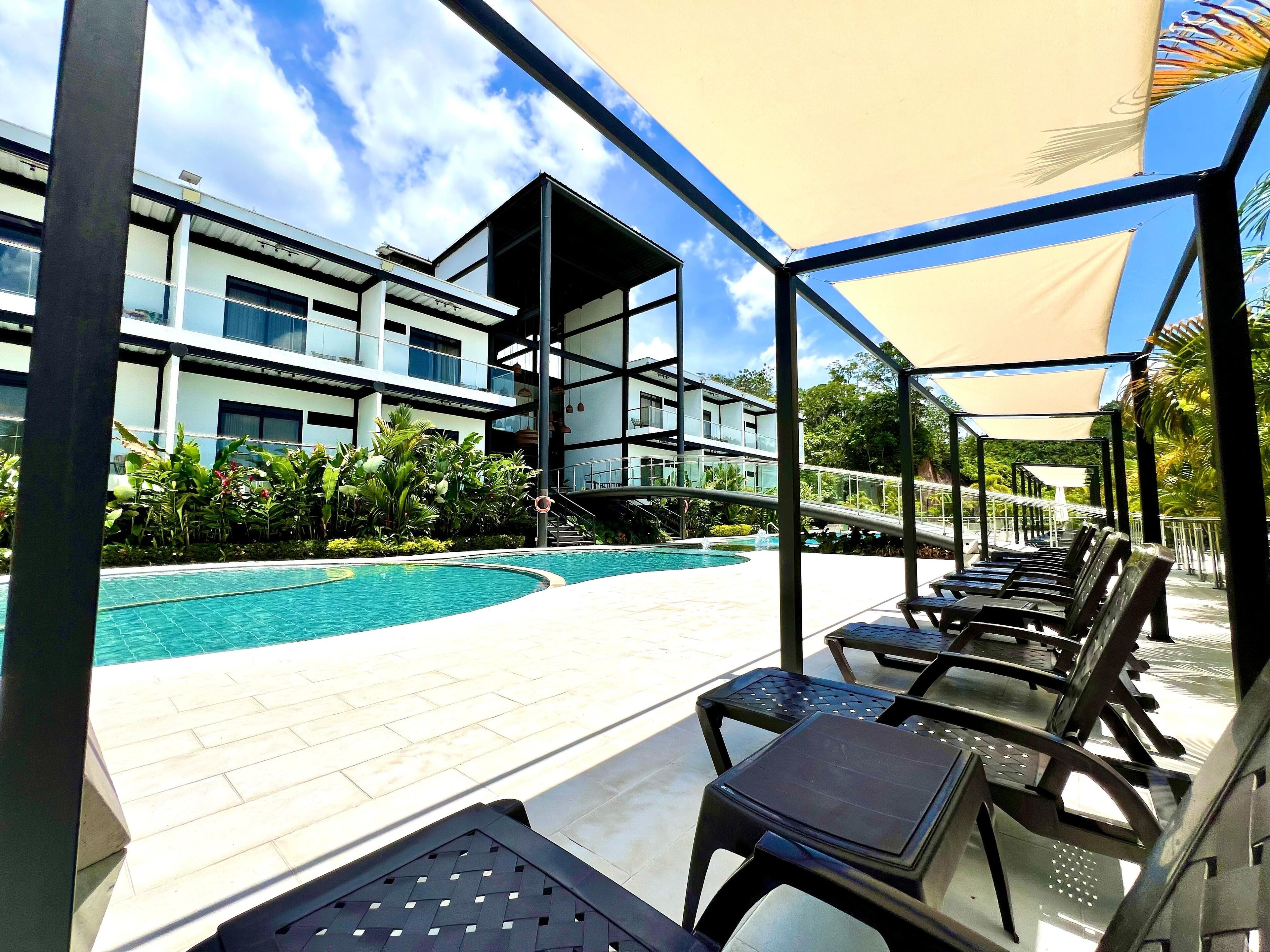 A poolside area with lounge chairs, a swimming pool, and a modern building with balconies.