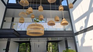 Interior de un edificio moderno con múltiples lámparas colgantes de mimbre, barandilla de vidrio y un cartel que dice 'DIAÑOS EN LORADA'.