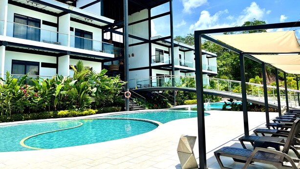 Un hotel moderno de varios pisos con piscina y zona de estar exterior.