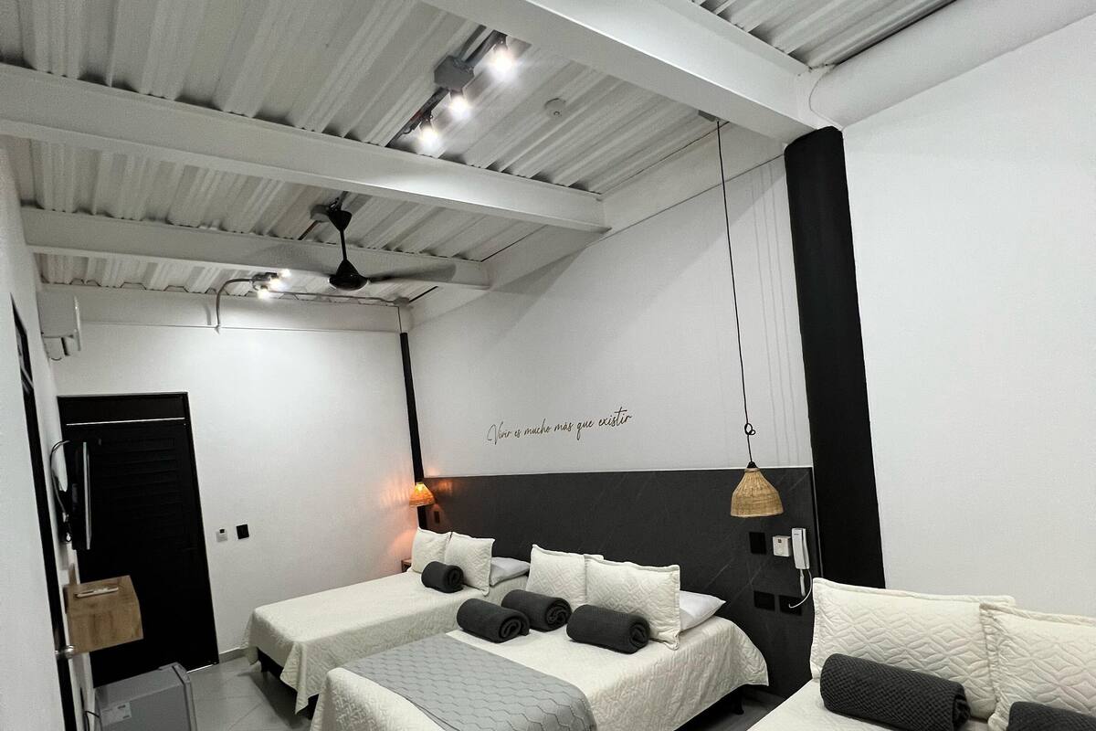 Een moderne hotelkamer met drie bedden, een plafondventilator en een wandlamp.